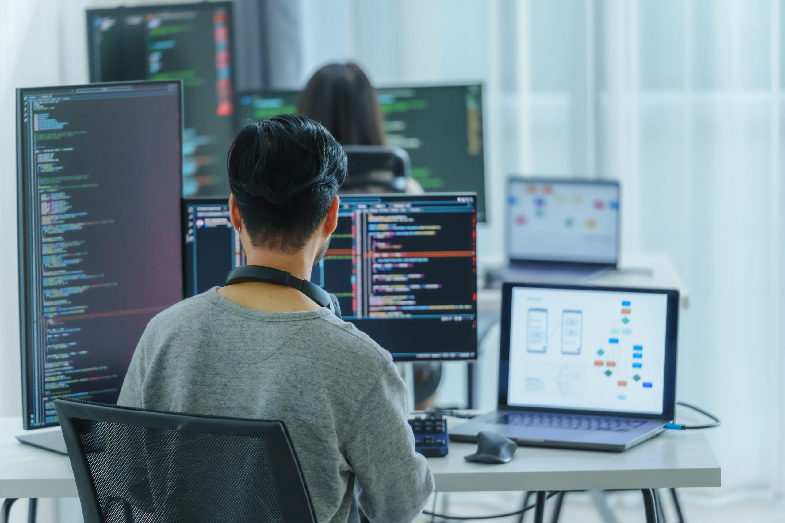 Asian software developers working on multiple screens displaying code and application diagrams in a modern office